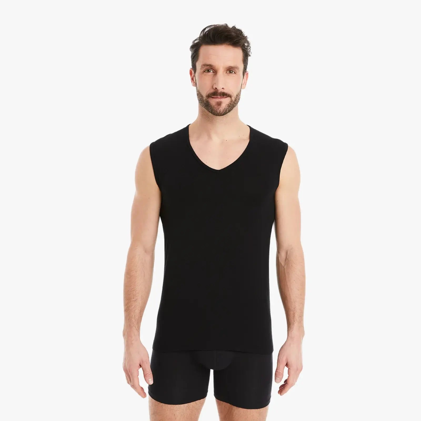 Schwarzes ärmelloses Herren Unterhemd mit V-Ausschnitt. Micro-Modal Stoff, weiter Ausschnitt, hoher Tragekomfort. Selbstbewusster Mann schaut direkt in die Kamera, Arme entspannt seitlich vom Körper. #farbe_schwarz