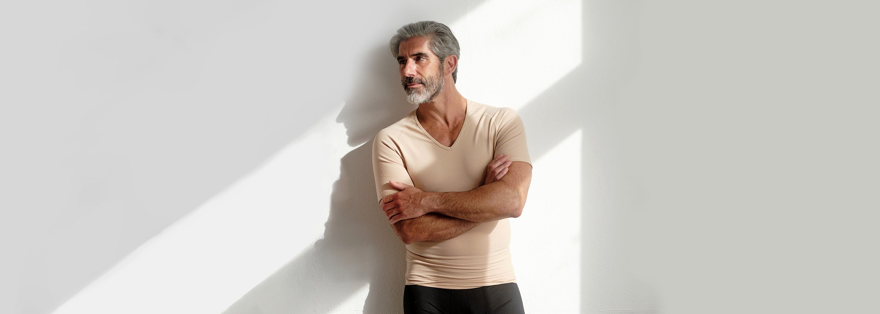 Mann im besten Alter in hautfarbenem Business-Unterhemd mit V-Ausschnitt genießt die Sonneneinstrahlung. Unsere Business-Unterhemden, aus feinstem Modal für ein natürlich weiches Gefühl auf der Haut, bieten Komfort und Stil für den geschäftigen Alltag.