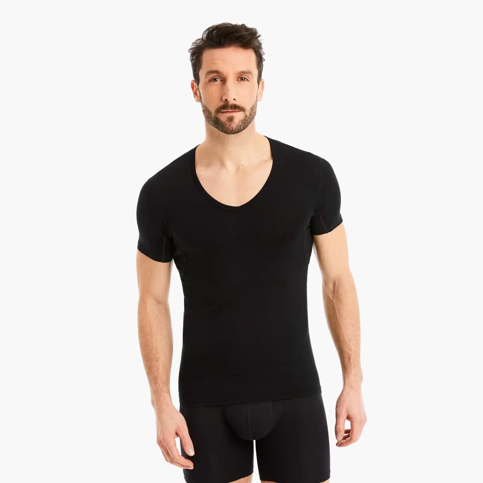 Selbstbewusster Mann schaut in die Kamera, trägt schwarzes Funktionsunterhemd Herren mit Einsätzen. Reduziert Schweißflecken, Slim-Fit Schnitt, hoher Tragekomfort. #farbe_schwarz