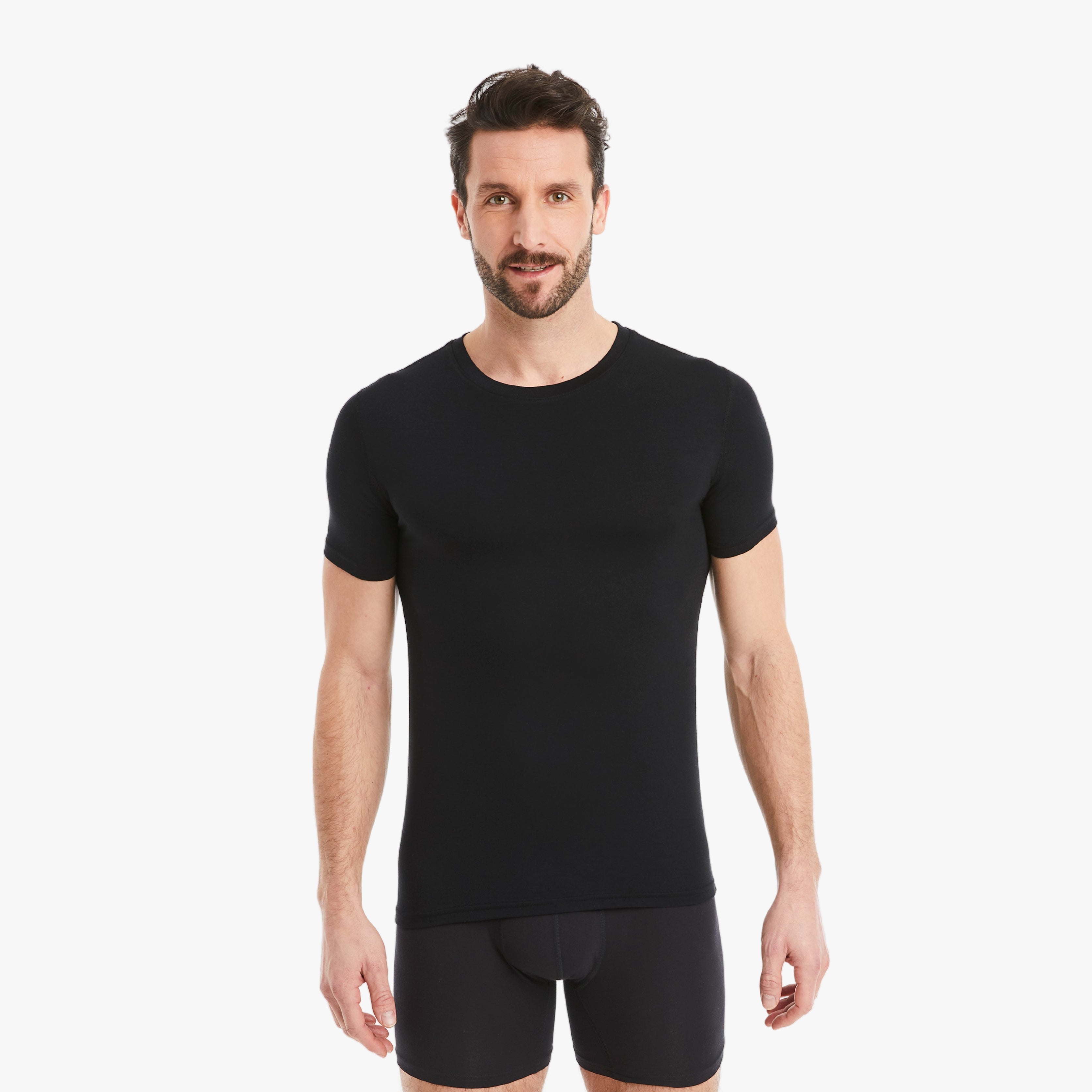 Schwarzes Herren Unterhemd Kurzarm Rundhals. Micro-Modal Stoff, hergestellt in Europa, hoher Tragekomfort. Selbstbewusster Mann schaut selbstbewusst in die Kamera, Arme entspannt an der Seite. #farbe_schwarz
