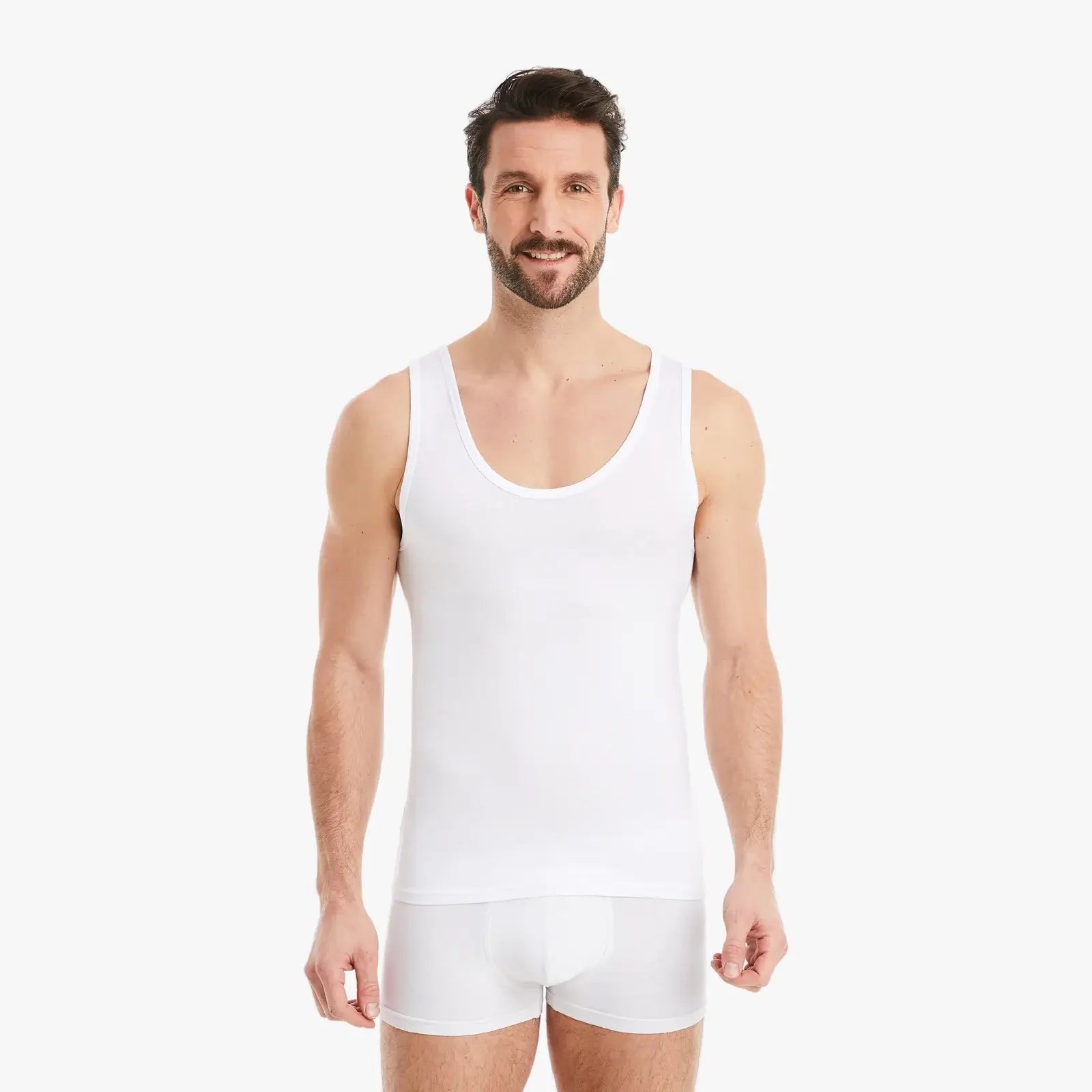 Selbstbewusster Mann mit entspannten Armen seitlich lacht in die Kamera. Er trägt ein weißes Herren Unterhemd Tank-Top aus Micro-Modal Stoff im Slim Fit. #farbe_weiß