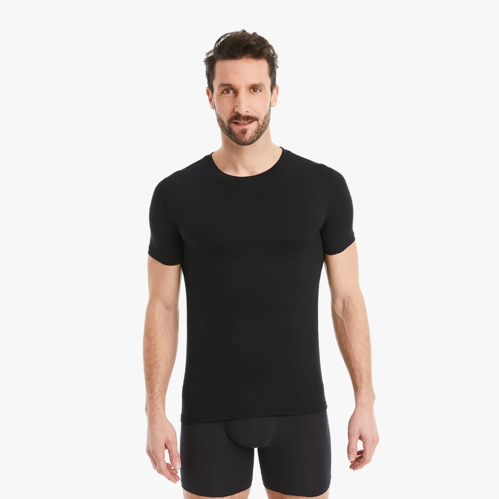 Schwarzes Herren Unterhemd Kurzarm Rundhals. Micro-Modal Stoff, hergestellt in Europa, hoher Tragekomfort. Selbstbewusster Mann schaut selbstbewusst in die Kamera, Arme entspannt an der Seite. #farbe_schwarz