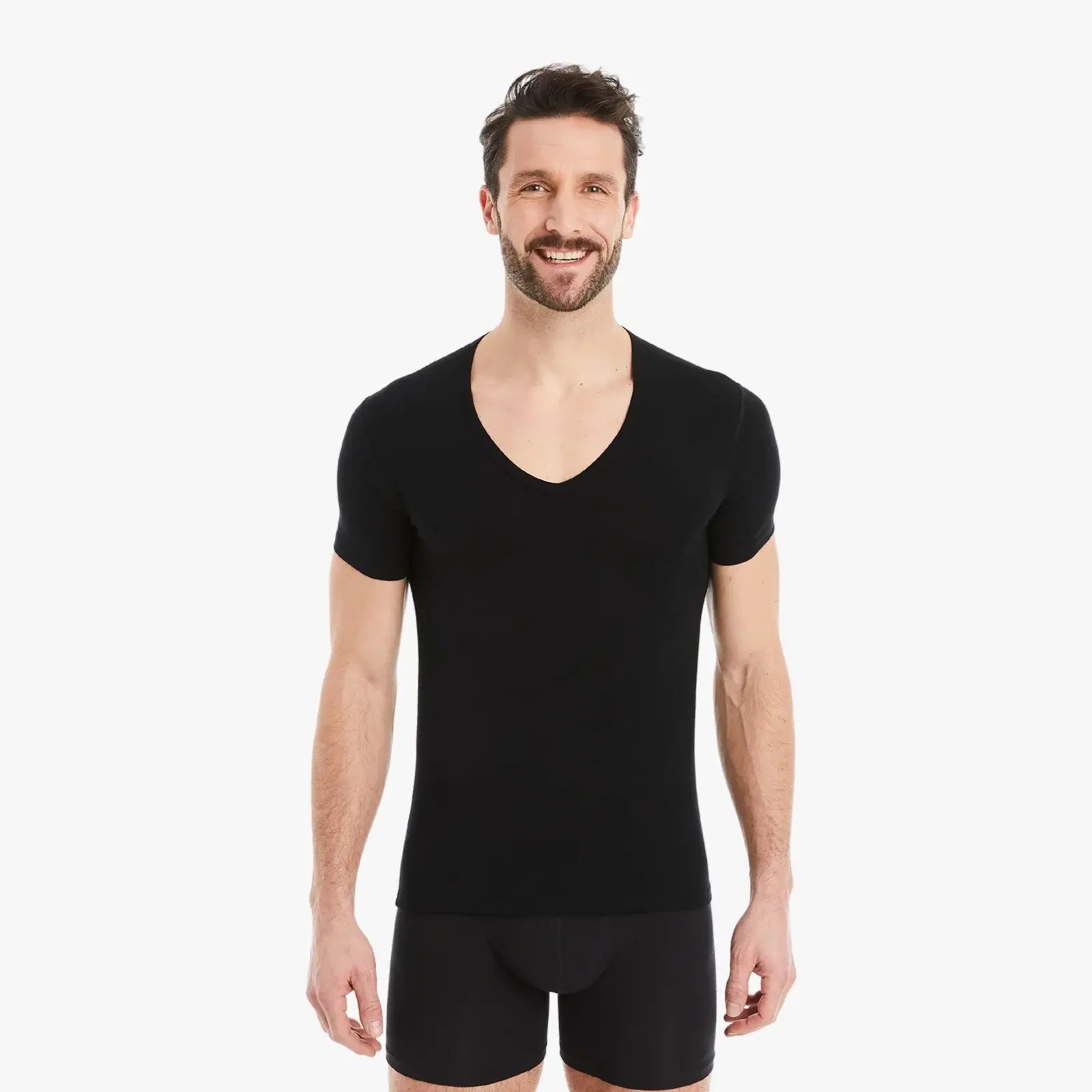 Selbstbewusster Mann lächelt in Kamera, trägt schwarzes Herren Unterhemd Kurzarm V-Ausschnitt aus Micro-Modal Stoff, Slim Fit, mit entspannten Armen seitlich. #farbe_schwarz