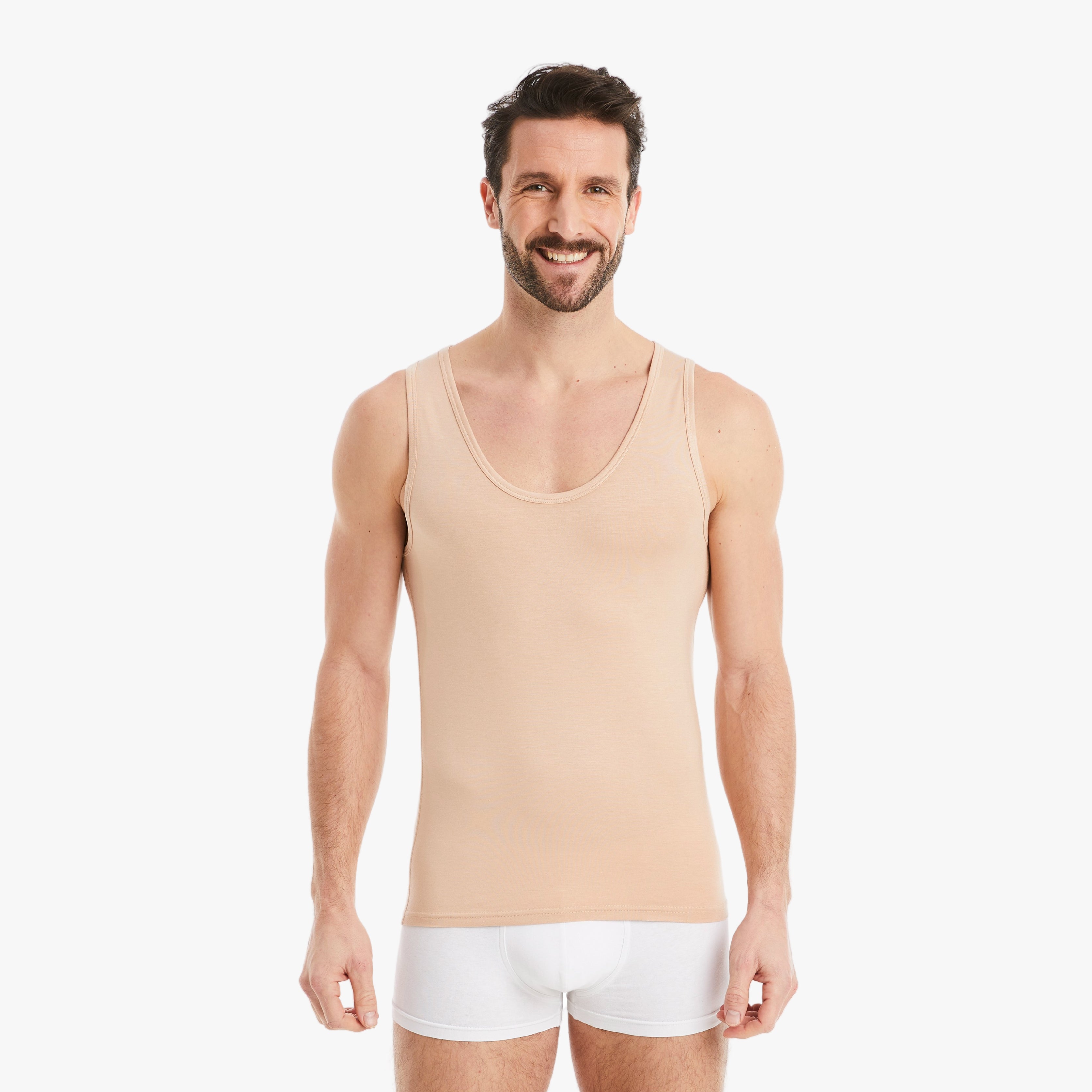 Selbstbewusster Mann lacht in Kamera, trägt hautfarbenes Herren Unterhemd Tank-Top aus Micro-Modal Stoff, Slim Fit, mit entspannten Armen seitlich. #farbe_nude