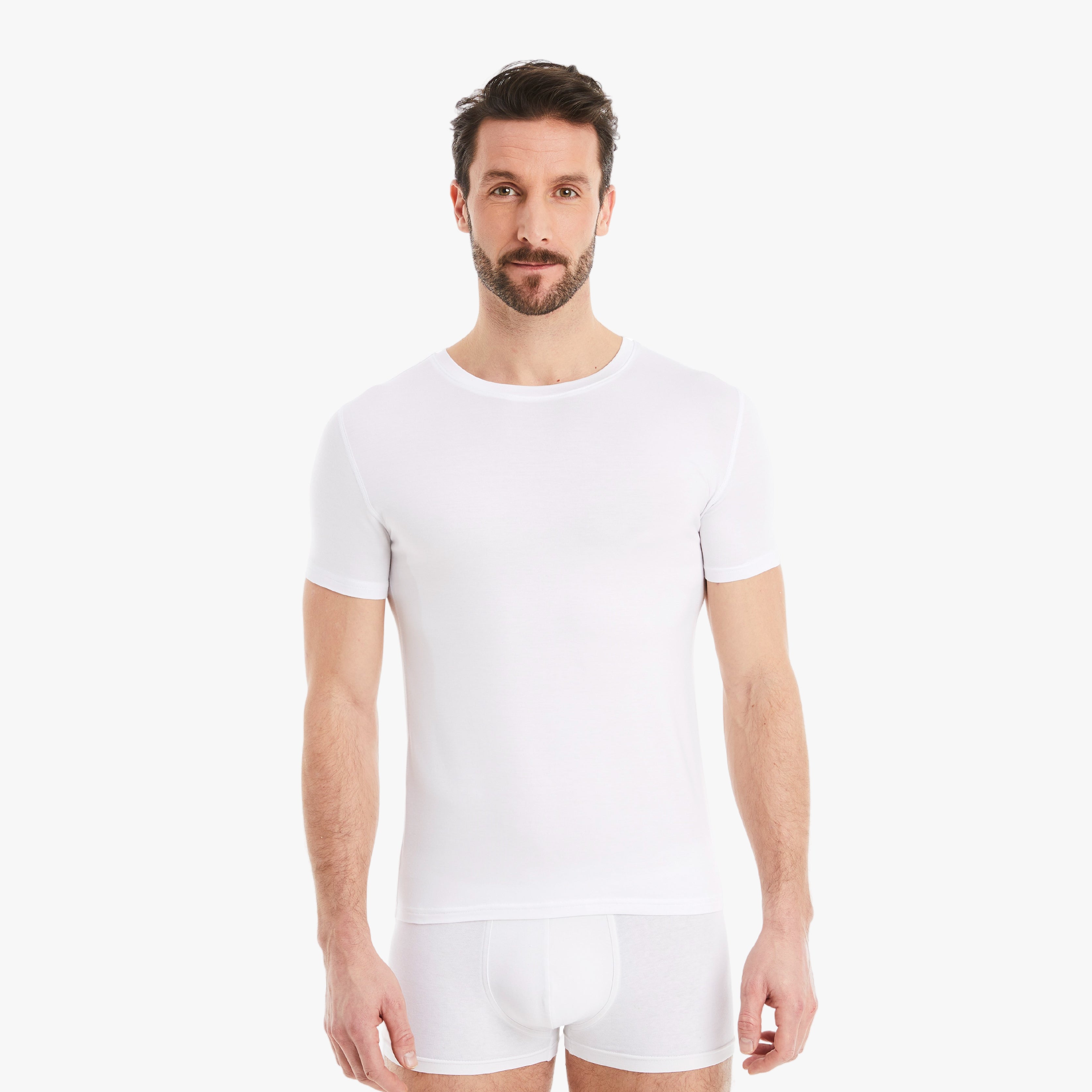 Weißes Herren Unterhemd Kurzarm Rundhals. Micro-Modal Stoff, hergestellt in Europa, hoher Tragekomfort. Selbstbewusster Mann, Arme entspannt seitlich vom Körper, schaut direkt in die Kamera. #farbe_weiß