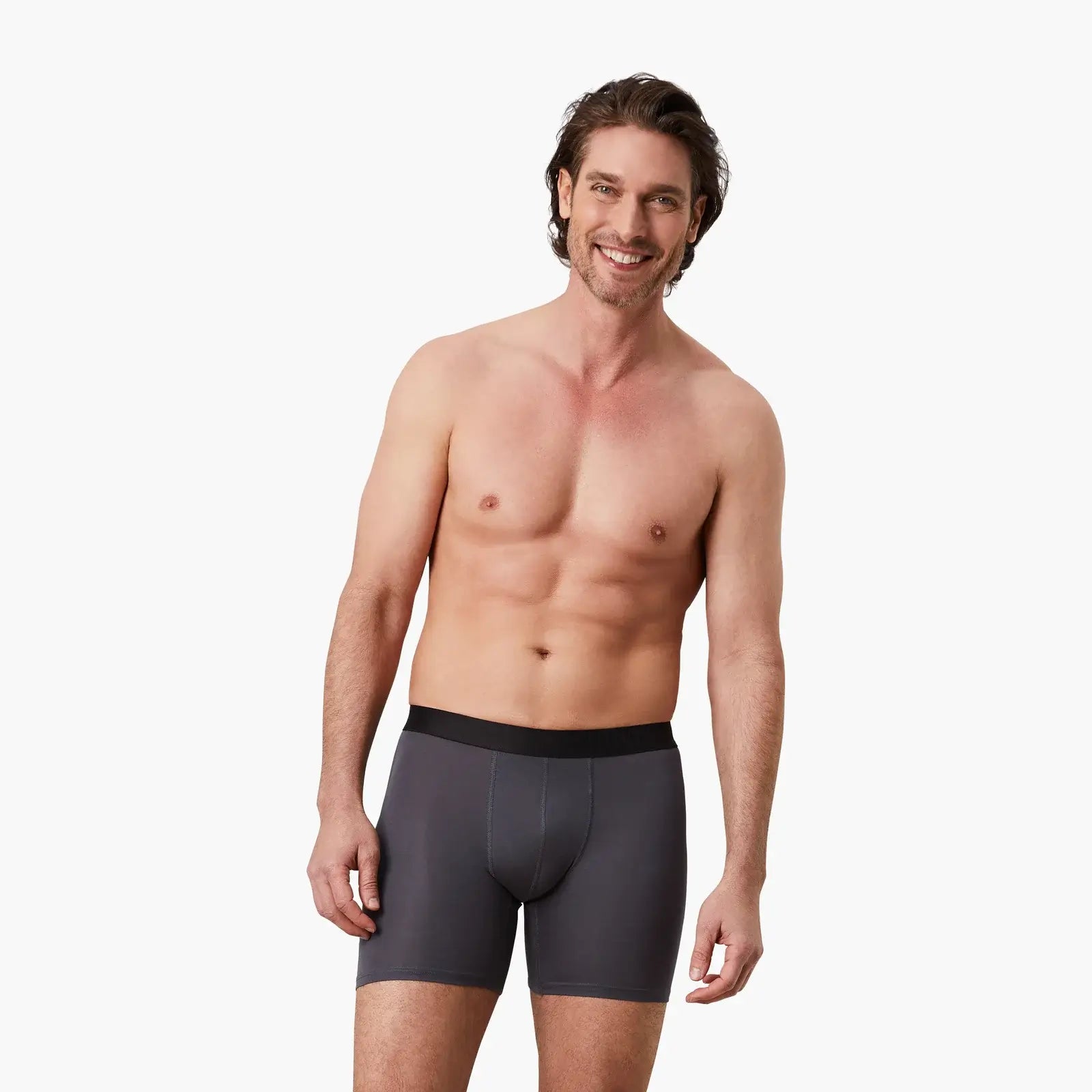 Zufriedener Mann trägt graue Anti-Schweiß Boxershorts Herren in Größe M. 100% Schutz vor Schweißflecken durch innovative 3-Lagen Technologie. Zertifizierter Tragekomfort, während er entspannt in die Kamera lächelt.#farbe_grau, #farbe_schwarz/blau/grau