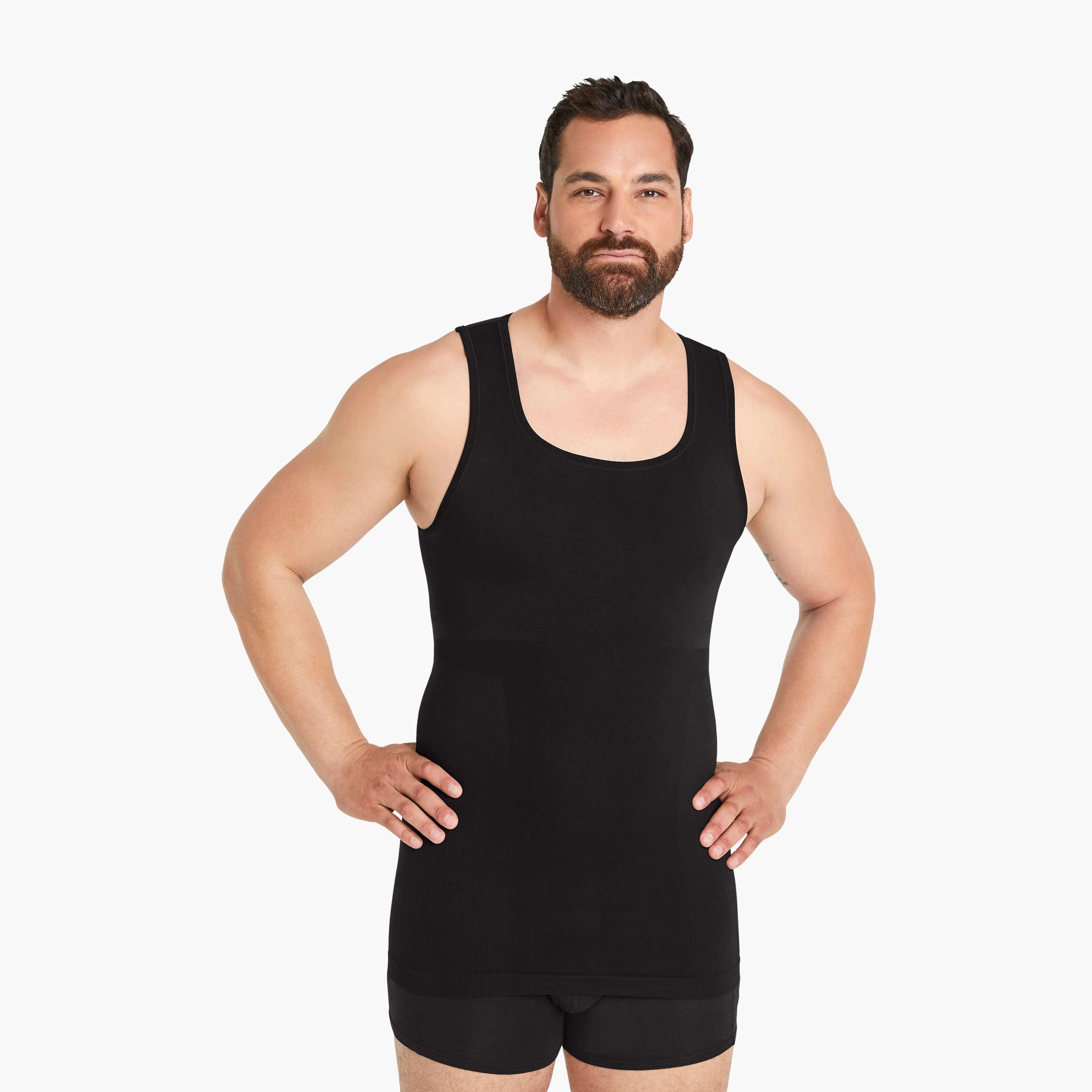 Ein Mann in einem Seamless Shapewear Tank-Top für Herren schaut selbstbewusst in die Kamera, die Hände in die Hüften gestemmt. Mit innovativer Seamless Technologie für Tragekomfort und Bauch-weg Effekt. #farbe_schwarz