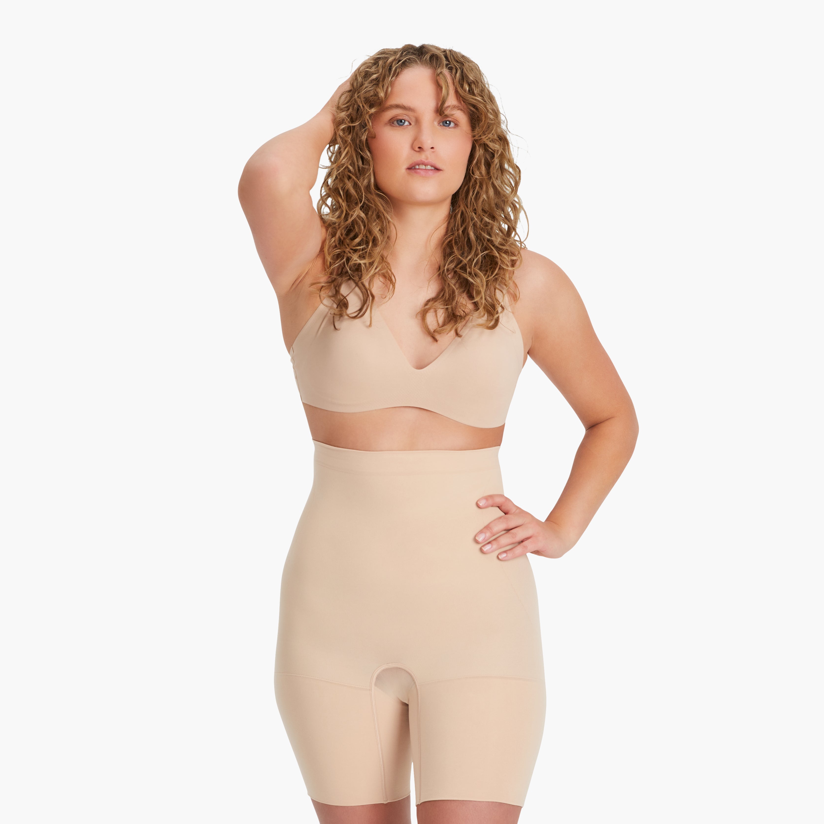 Blonde Frau mit lockigem Haar trägt hautfarbene Shapewear Shorts und fühlt sich sichtlich wohl. #farbe_nude