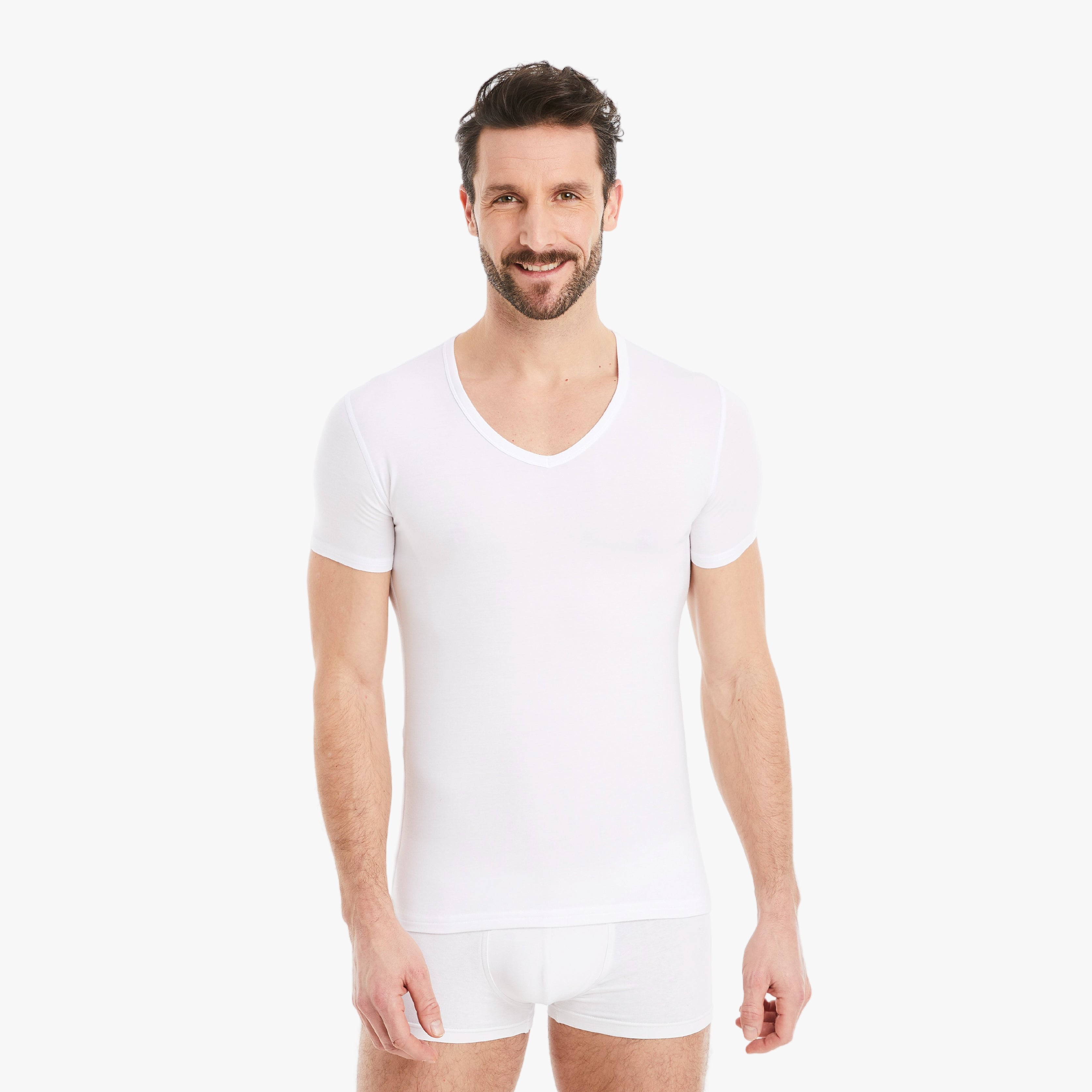 Selbstbewusster Mann lächelt in die Kamera, trägt ein weißes Herren Unterhemd Kurzarm V-Ausschnitt aus Micro-Modal Stoff, Slim Fit für optimalen Tragekomfort, mit entspannten Armen seitlich. #farbe_weiß